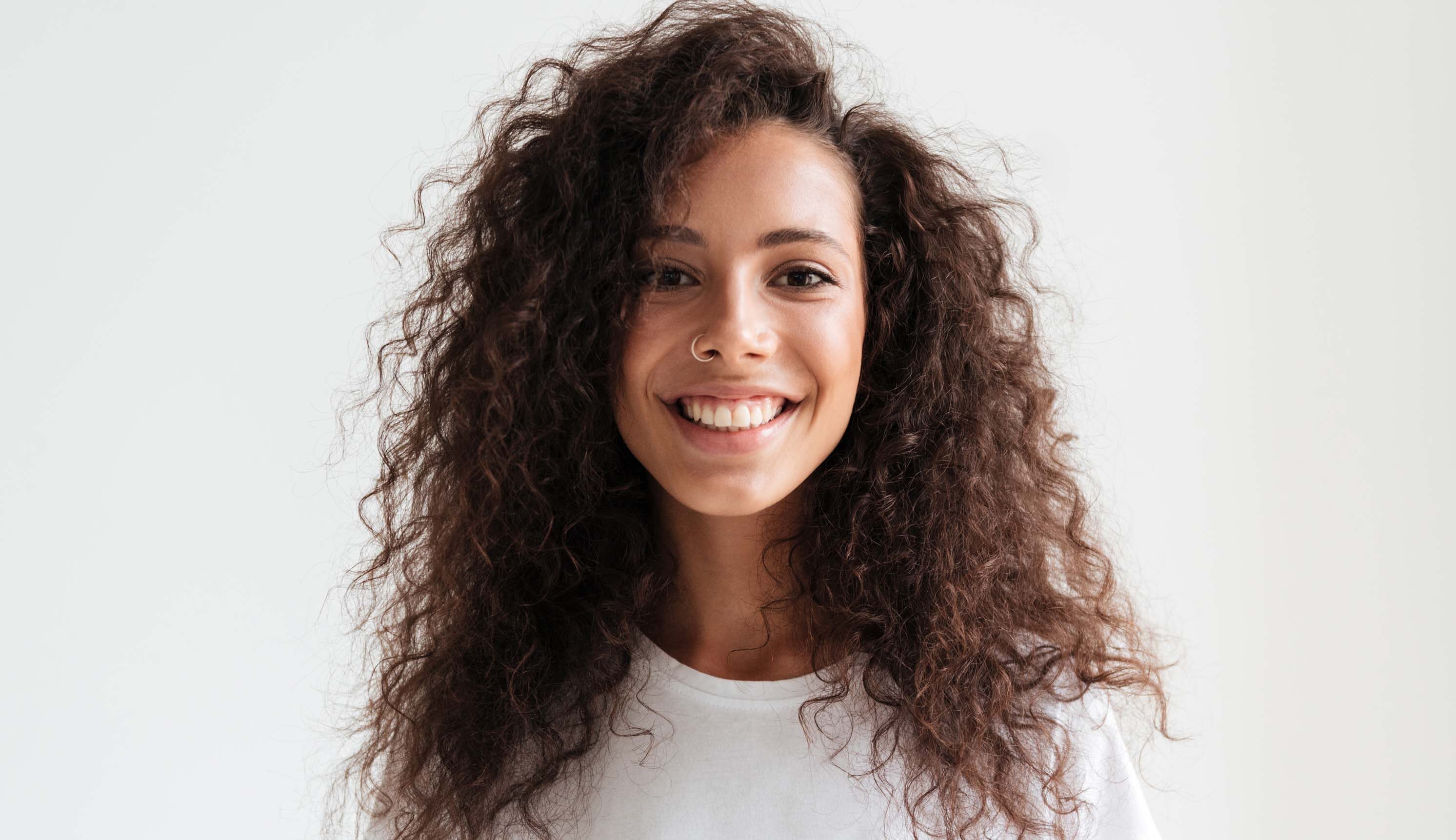 Woman smiles, proud of her broad, brilliant smile, thanks to Invisalign and porcelain veneers in NYC.